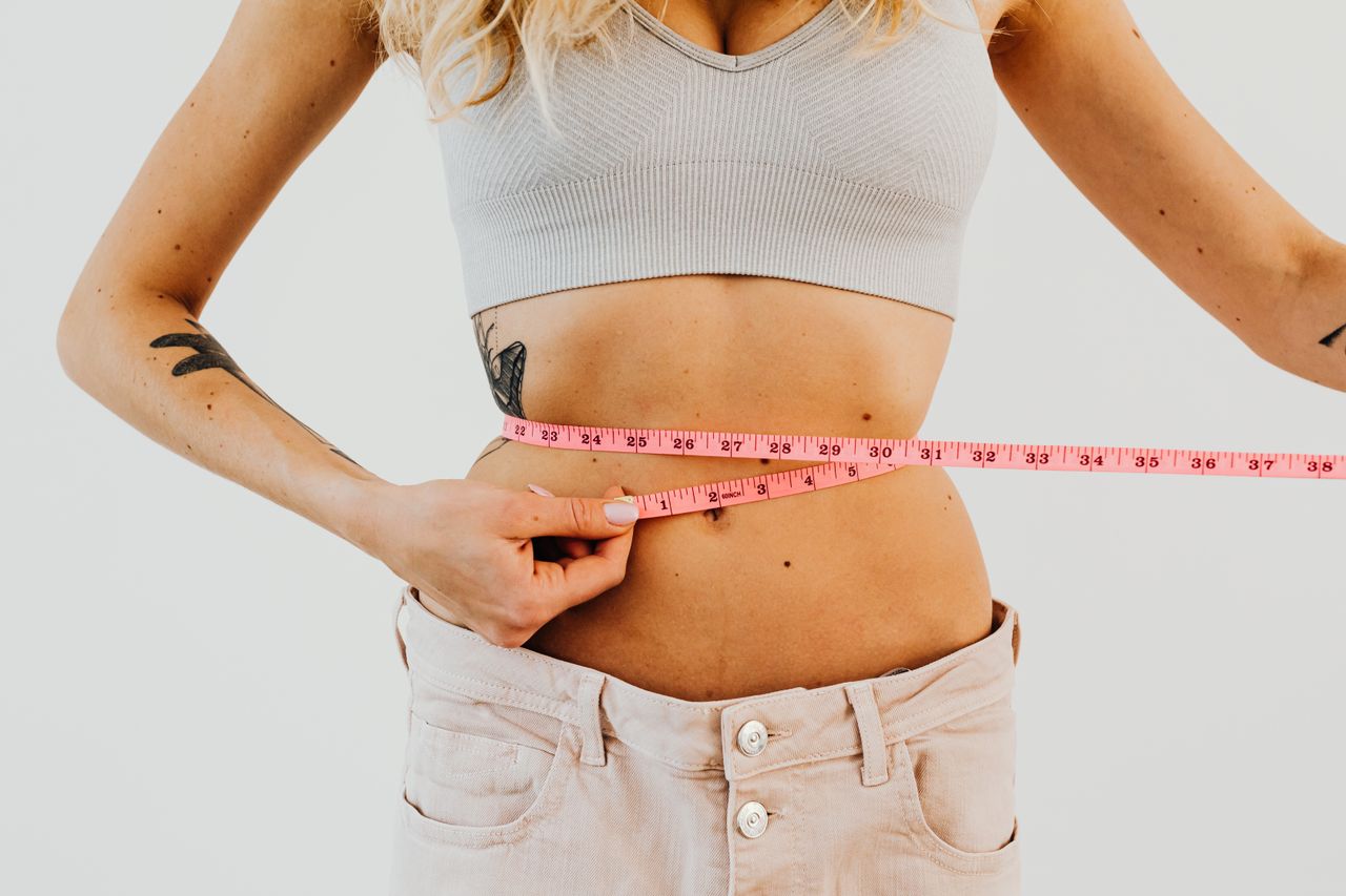 Crafting Captivating Headlines: Your awesome post title goes here Close-up of woman in sports bra measuring waist with pink tape for fitness goals.