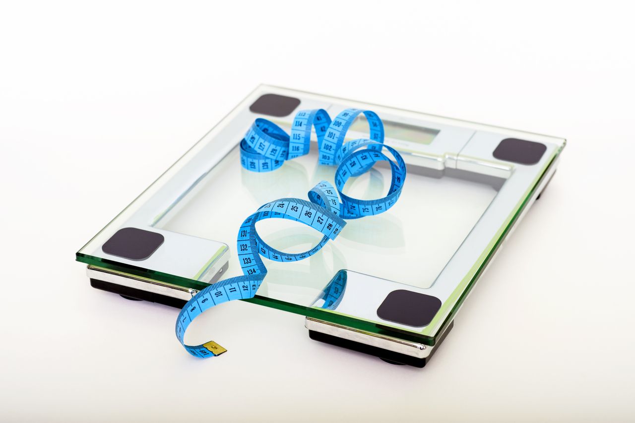 About A digital glass weighing scale with a blue measuring tape, symbolizing weight management.
